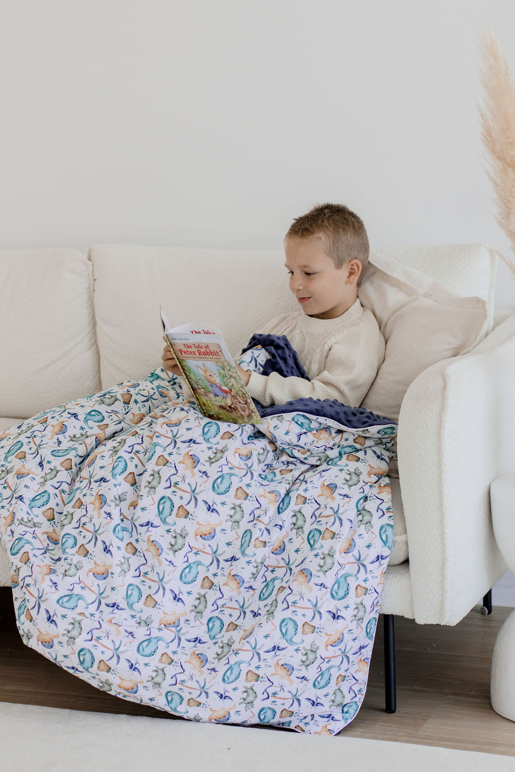 Child reading a book while wrapped in Wild Dinosaurs weighted blanket
